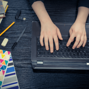 An image of a person's hands typing at their laptop with school supplies beside them on the desk. 