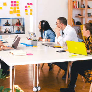 Office workers around a table looking at remote workers on a computer screen