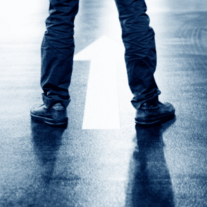 Person standing on empty road in front of a directional arrow