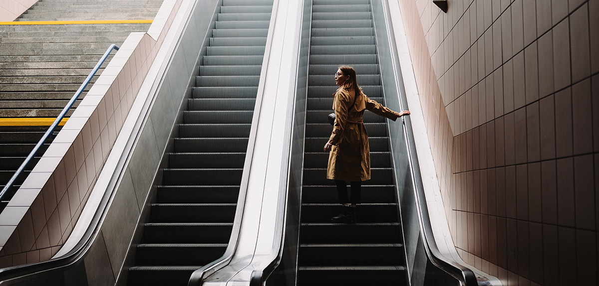 Beautiful young woman in trench coat stands on an escalator in the subway.